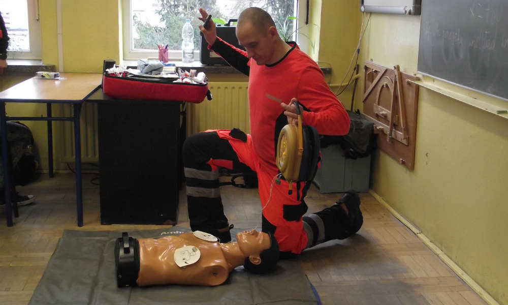 Ratownik medyczny prezentujący na manekinie defibrylację za pomocą defibrylatora