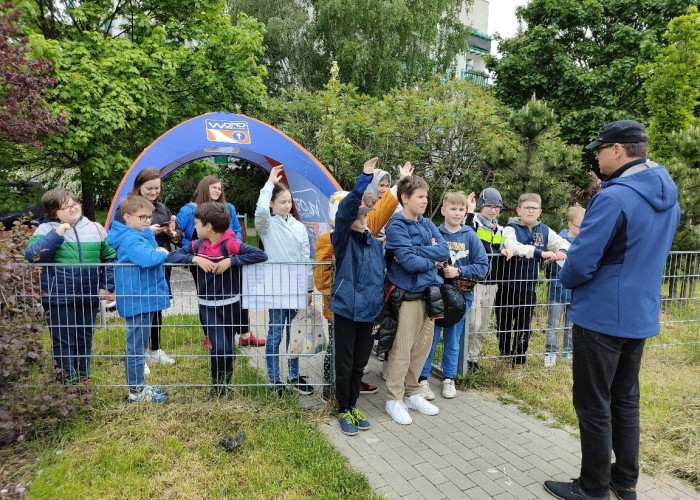 Zdjęcie 1. Uczestnicy „zajęć teoretycznych” z bezpieczeństwa w ruchu drogowym z prowadzącym zajęcia praktyczne Egzaminatorem z WORD w Warszawie Sławomirem Bakalarskim na miasteczku rowerowym przy ul. Kazury. (Zdjęcie źródło: WORD w Warszawie)