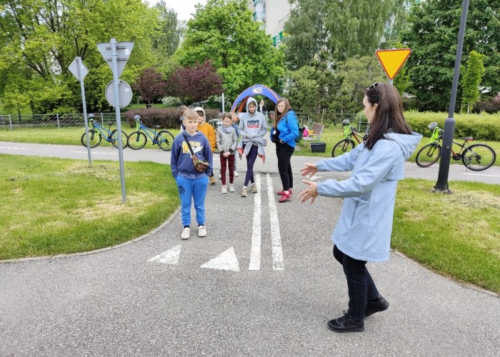 Zdjęcie 3. Uczestnicy „zajęć teoretycznych” z bezpieczeństwa w ruchu drogowym z prowadzącą zajęcia praktyczne Egzaminatorką z WORD w Warszawie Emilią Liberacką na miasteczku rowerowym przy ul. Kazury. (Zdjęcie źródło: WORD w Warszawie)