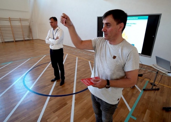 Zdjęcie 4. Osoby prowadzące zajęcia edukacyjne z dziećmi, od lewej: Egzaminator z WORD w Warszawie Sławomir Bakalarski i Burmistrz Dzielnicy Ursynów Robert Kempa prezentujący ulotkę informacyjną oraz wlepkę z numerami alarmowymi do naklejania na hulajnogę elektryczną lub rower. (Zdjęcie źródło: Urząd Dzielnicy Ursynów m. st. Warszawy).