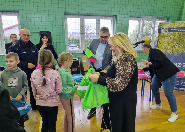 Zdjęcie 4. Artur Rola – Dyrektor Delegatury  Urzędu Marszałkowskiego Województwa Mazowieckiego w Wołominie, Agnieszka Gryglas – Zastępca Burmistrza Miasta i Gminy Tłuszcz, aspirant sztabowy Grzegorz Moszyński – Zastępca Naczelnika Wydziału Ruchu Drogowego w Wołominie wręczają uczniom ze SP w Miąsem zestawy elementów odblaskowych. (Zdjęcie źródło: WORD w Warszawie)