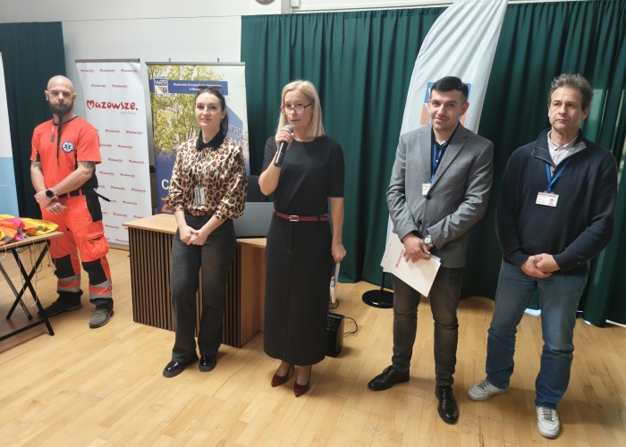 Zdjęcie 2. Przedstawienie harmonogramu spotkania: (stoją od lewej) Pan Michał Kamiński Ratownik Medyczny z SPZOZ MEDITRANS w Warszawie, Pani Emilia Liberacka Egzaminator z WORD w Warszawie, Pani Mirosława Lewandowska – Dyrektor SP nr 206 w Warszawie, Pan Kacper Wojdalski i Pan Marek Wagner – przedstawiciele Urzędu Marszałkowskiego Województwa Mazowieckiego w Warszawie. (zdjęcie źródło: WORD w Warszawie).