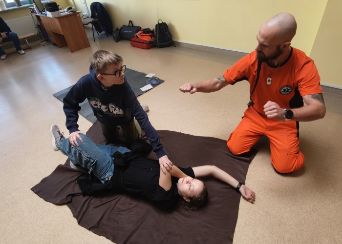 Zdjęcie 9. Uczniowie ze SP nr 206 w Warszawie oraz Pan Michał Kamiński Ratownik Medyczny z SPZOZ MEDITRANS w Warszawie podczas ćwiczenia tzw. „pozycji bezpiecznej bocznej ustalonej” u osoby nieprzytomnej oddychającej w ramach panelu „pierwsza pomoc”. (zdjęcie źródło: WORD w Warszawie).