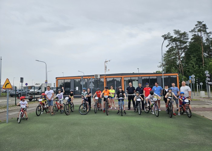 Zdjęcie 11. Wspólne pamiątkowe zdjęcie uczestników jazd rowerem po miasteczku ruchu drogowego oraz Policjantów z KP Policji z Nowego Dworu Mazowieckiego na terenie MCBRD w Modlinie podczas „Rowerowego Dnia Dziecka” (Zdjęcie źródło: KPP a Nowym Dworze Mazowieckim).