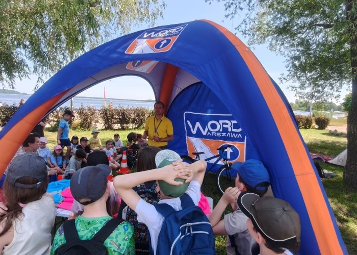 Zdjęcie 5. Dzieci ze szkół podstawowych z Gminy Nieporęt oraz Egzaminator z WORD w Warszawie Pan Sławomir Bakalarski podczas zajęć edukacyjnych dotyczących bezpiecznego uczestnictwa w ruchu drogowym pieszych, pasażerów, rowerzystów i hulajnogistów (zdjęcie źródło: WORD w Warszawie).