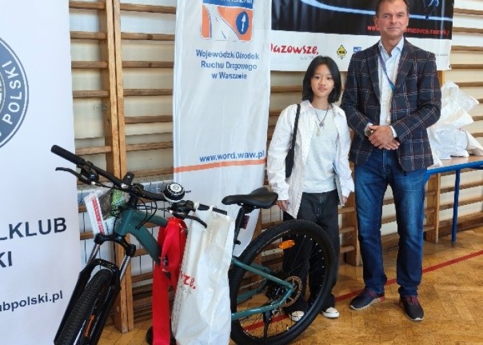 Zdjęcie 5. Wspólne pamiątkowe zdjęcie Nguyen Minh Chau Giang - najlepszej uczennicy biorącej udział w Portalu Bezpieczne Mazowsze ze SP w Otrębusach oraz oraz Sławomira Bakalarskiego - Egzaminatora prawa jazdy 
z Wydziału Szkoleń i BRD Wojewódzkiego Ośrodka Ruchu Drogowego w Warszawie. (zdjęcie źródło: WORD w Warszawie).