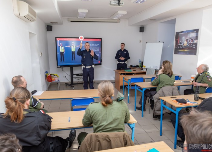Zdjęcie 1. Na zdjęciu: uczestnicy części teoretycznej szkolenia z kierowania ruchem drogowym - Harcerze Chorągwi Stołecznej Związku Harcerstwa Polskiego oraz sierżant Patryk Cieśliński (z lewej) i sierżant sztabowy Krzysztof Dygnos - Policjanci z WRD Komendy Stołecznej Policji (Zdjęcie źródło: Marek Szałajski - Komenda Stołeczka Policji).