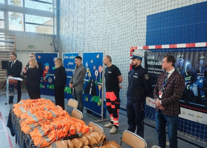 Zdjęcie 1. Rozpoczęcie spotkania - przywitanie i przedstawienie zaproszonych gości, uczniów i nauczycieli ze SP w Kołbieli przez Panią Dyrektor – Małgorzatę Szerszeń (z mikrofonem). Na zdjęciu od lewej: Pan Sylwester Winek – Wójt Gminy Kołbiel, Pan Artur Rola – Dyrektor Delegatury Urzędu Marszałkowskiego Województwa Mazowieckiego w Wołominie, Pani Małgorzata Szerszeń – Dyrektor Szkoły, Pani Katarzyna Szymańska i Pan Kacper Wojdalski – przedstawiciele Urzędu Marszałkowskiego Województwa Mazowieckiego w Warszawie, Pan Piotr Żak - ratownik medyczny z SPZOZ MEDITRANS w Warszawie, sierżant Piotr Świątek – Policjant z Komendy Powiatowej Policji w Otwocku oraz Pan Sławomir Bakalarski – Egzaminator z Wojewódzkiego Ośrodka Ruchu Drogowego w Warszawie. (zdjęcie źródło: WORD w Warszawie).